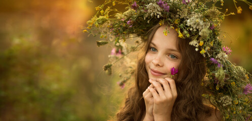 Cute smiling little girl  with flower wreath on the meadow at the farm. Portrait of adorable small kid outdoor.