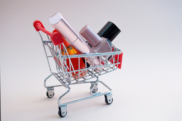 Front view of a shopping cart with makeup products on a pink background. Cosmetic shopping concept.