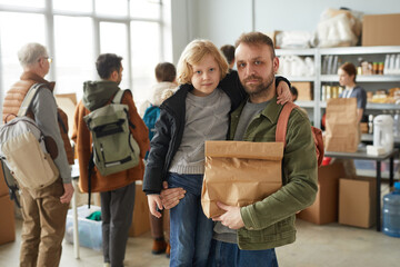 Waist up portrait of father and son holding food donations at volunteer center for refugees and...