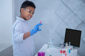 A boy in a lab coat working with test tubes and looking involved