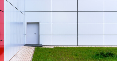 white wall with grey door near panoramic windows with red decorative line at paved sidewalk and green flowerbed