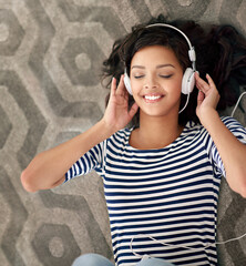 The sweet sounds of music. High angle shot of a young woman listening to music on her cellphone while lying on the floor.