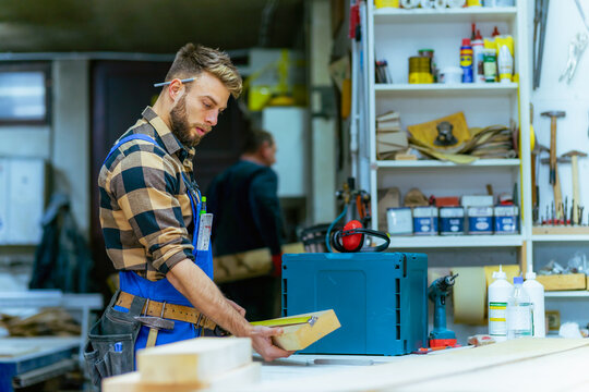 Portrait of young handsome caucasian carpenter who measures a board at the workshop