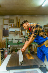Bearded carpenter working on machine for straighten wood boards