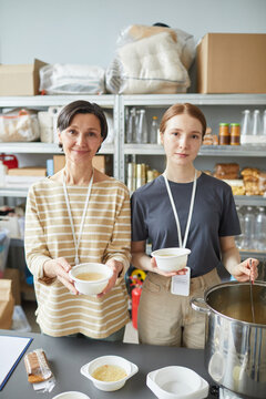Vertical portrait of two Caucasian women volunteering at help center and smiling at camera