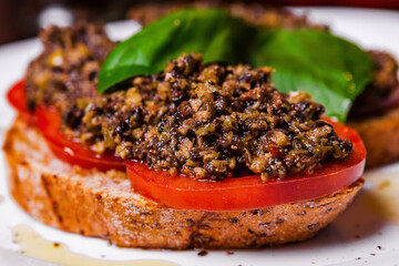 Bruschetta with capers, olives and tomatoes on a white plate