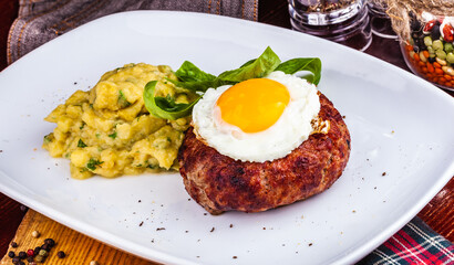 Grilled steak with fried egg and mashed potatoes on white plate