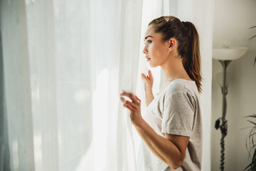 Fototapeta na wymiar Woman Feeling Worried While Standing Near The Window At Home