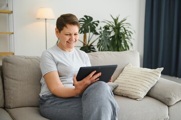 people, technology and internet concept - happy middle aged woman with tablet pc computer at home.