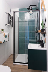 Interior of modern bathromm with green tiles in shower cabin, Bathroom sink with cabinet and pattern tile in stylish design. Vertical.