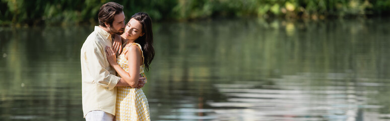 young couple in summer clothes hugging near river, banner.