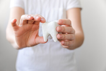 Health dental care concept. Woman hand holding white healthy tooth model isolated on white background. Teeth whitening, dental oral hygiene, teeth restoration, dentist day