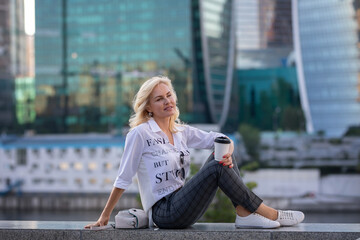 Fototapeta premium blonde woman resting with a cup of coffee on the background of skyscrapers