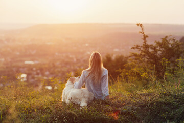 Fototapeta na wymiar Girl with her golden retriever dog sitting on hill during summer sunset watching a beautiful landscape.