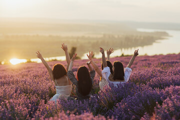 Girlfriends with hands up at sunset. They having picnic in the lavender field and enjoying...