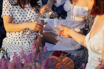 A woman pouring wine in glasses. Picnic in the lavender field. Close up.