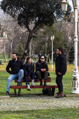 Obraz premium Four young people sitting on bench and talking each others. Friendship, fun and joy concept.