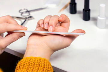 Young Caucasian woman making self manicure at home with the help of nail file and other tools for nail procedures. - 498640637