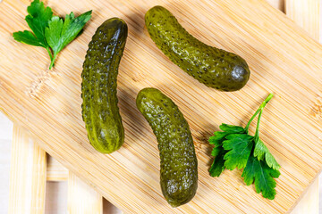 Tasty homemade green pickled cucumbers with fresh parsley on light wooden cutting board background in the kitchen.
