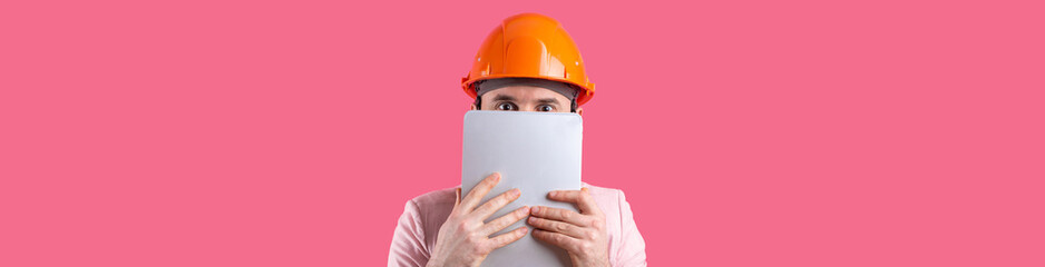 Portrait of young construction engineer wear orange hard hat, in a pink jacket standing on red studio background. A man with a tablet in his hands.