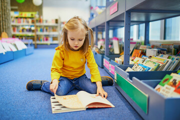 4 year old girl sitting on the floor in a municipal library and reading a book
