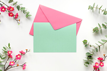 Blank mint green postcard with pink envelope. Red plum flowers on twigs, fresh eucalyptus leaves. Chinese new year design. Top view on off white background.