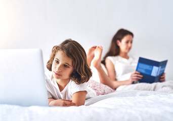 Engrossed in their own worlds. Cropped shot of a young girl using a laptop while her mom reads a...
