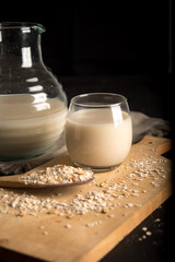 Transparent glass of Oat milk and oatmeal in spoon isolated on a wooden table with a dark background. a dark wooden board. A bottle of milk in the background