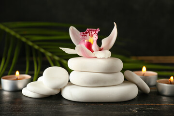 Spa stones with orchid flower and aroma candles on dark wooden background