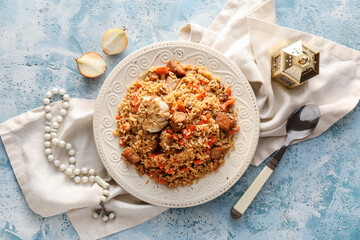 Plate of traditional pilaf with tasbih and fanoos lamp on color background