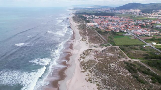 DRONE AERIAL FOOTAGE: Northern Littoral Natural Park in Esposende, Portugal. Sea, beach boulders, pebble shore, and waves. Sea waves breaking on rocks. Sunny beach with sand dunes and a cloudy sky.