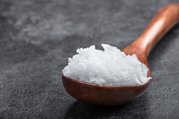 Pure natural sea salt crystal in wooden spoon on black stone background
