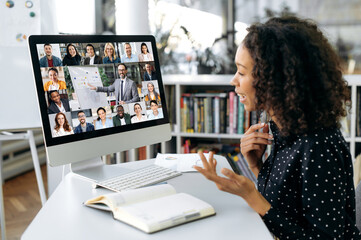 Fototapeta na wymiar Video conference. Successful African American woman, company worker, sits at a work desk in front of a computer, takes an online brainstorm, business conversation with multiracial group of people