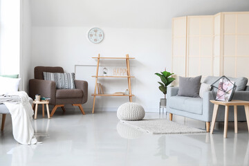 Interior of light living room with grey sofa, armchair and shelving unit