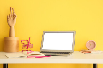 Modern laptop and stationery supplies on table near color wall