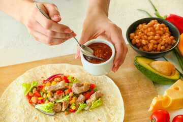 Woman adding sauce onto tasty burrito on white background
