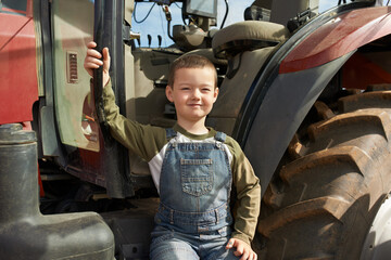 Fototapeta na wymiar You have to be this big to ride this. Portrait of a young boy sitting in front of a tractor.