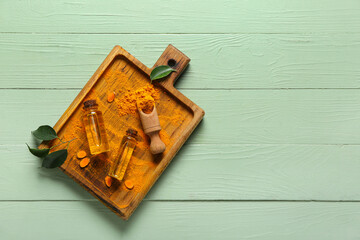 Bottles of oil, turmeric root and scoop with powder on green wooden background