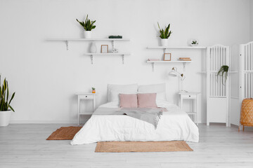 Interior of stylish bedroom with nightstands, folding screen, houseplants and lamp