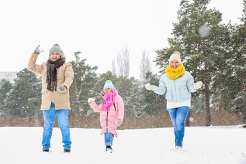 Little girl and her grandparents throwing snowballs on snowy winter day