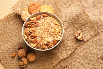 Bowl of healthy oatmeal with nuts on beige background