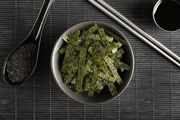 Bowl of chopped seaweed sheets and spoon of sesame on bamboo mat © Pixel-Shot