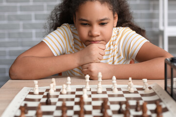 Little African-American girl playing chess during tournament in club