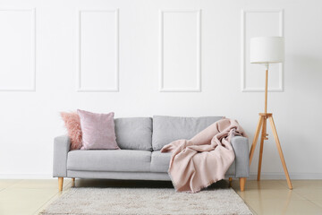 Stylish sofa and lamp near white wall