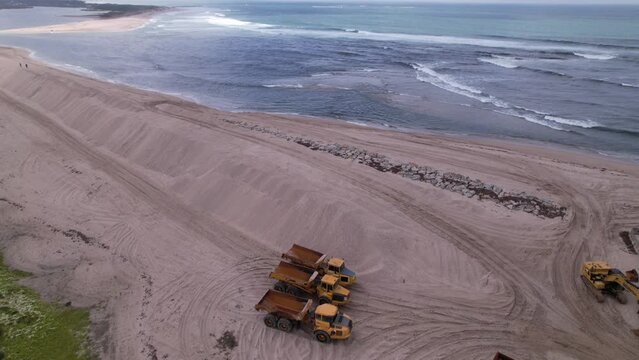 Esposende, Portugal, April 10, 2022: DRONE AERIAL FOOTAGE - The two sides of Restinga de Ofir. Esposende fishing harbor maintenance dredging. Dumper vehicles and rotating excavator parked on the sand.