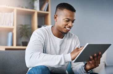 Just having a quick browse online. Shot of a handsome young man using his digital tablet while sitting on a sofa at home.