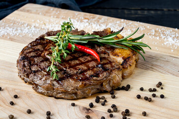 juicy Ribeye steak on the board with rosemary and red chili pepper macro close up