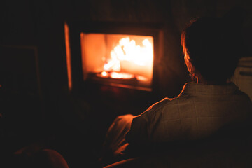 Cozy night in the cabin by the fireplace, fireplace burns in the scandinavian cottage chalet house, burning fire with charcoal and firewood, young woman with a drink reads book