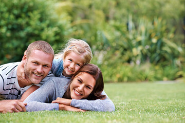 Fototapeta premium Having the best time with Mom and Dad. Portrait of a happy family of three lying outside on the grass.
