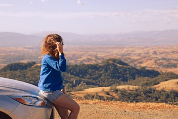 Young woman leaned to her car, stopped with a view during road trip